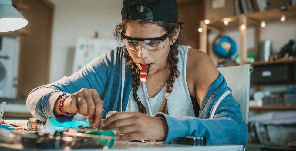 Teenage girl working on some engineering project at home.  Working table full of different tools and items needed for repairing electrical circuits.