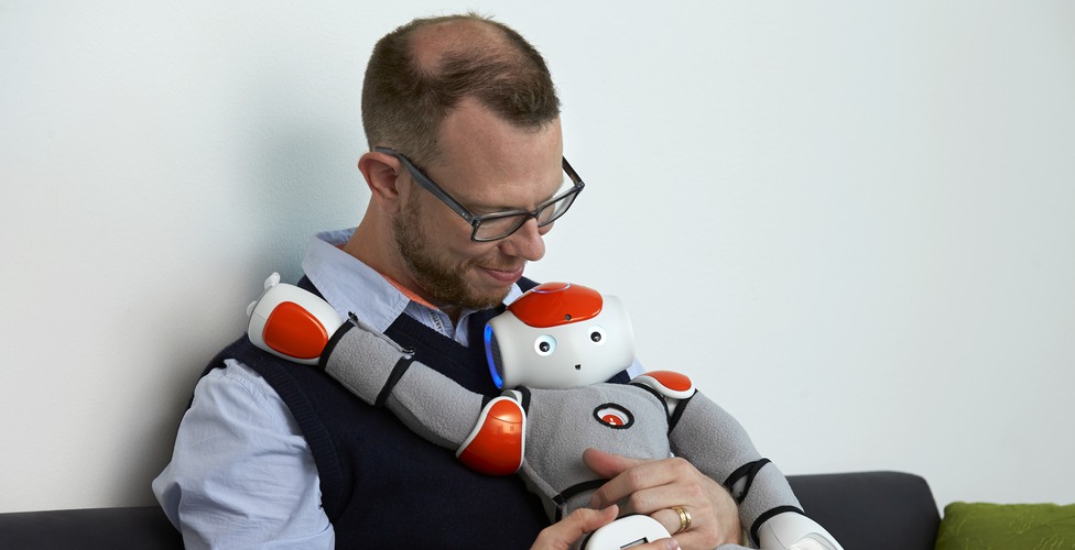 En social robot sitter i knät på en forskare och tittar mot betraktaren.