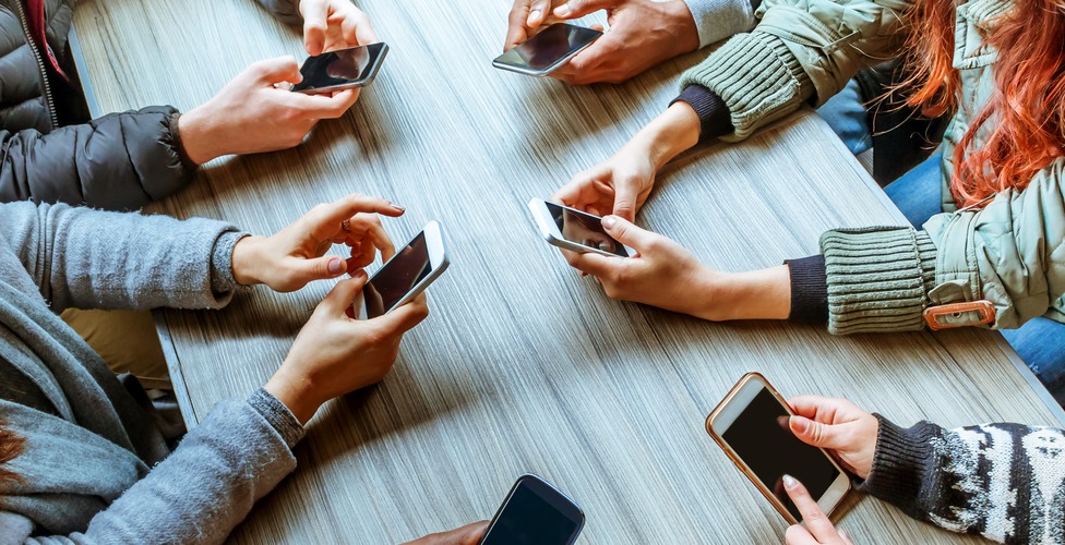 people using smart phones with touchscreen technology - cropped image top view of hands and phones of a group of friends sitting at a table