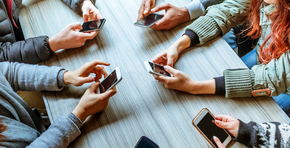 people using smart phones with touchscreen technology - cropped image top view of hands and phones of a group of friends sitting at a table