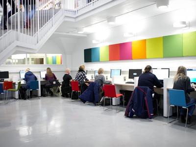 Sju studenter sitter och arbetar vid datorer i biblioteket