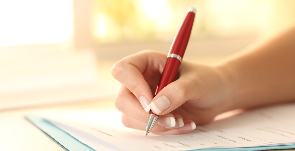 Close up of a woman hand using a pen to filling form on a table