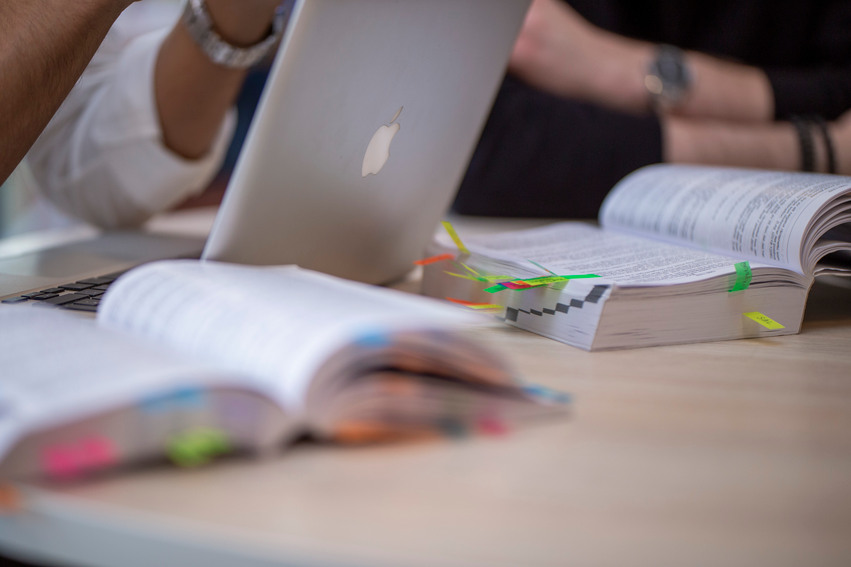 Kurslitteratur tillsammans med dator och penna när två studenter pluggar