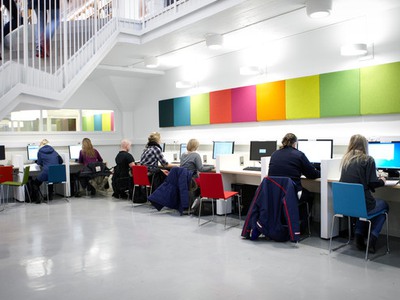 Sju studenter sitter och arbetar vid datorer i biblioteket